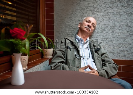 An elderly man sitting relaxed in a cafe waiting for a cup of coffee
