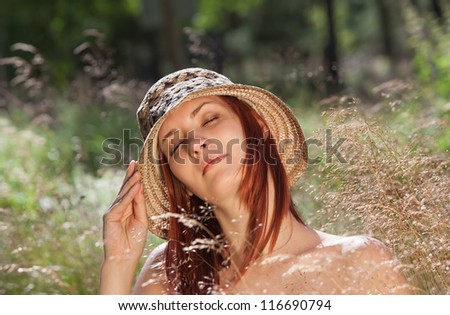 Woman in a hat with closed eyes in the grass on forest background