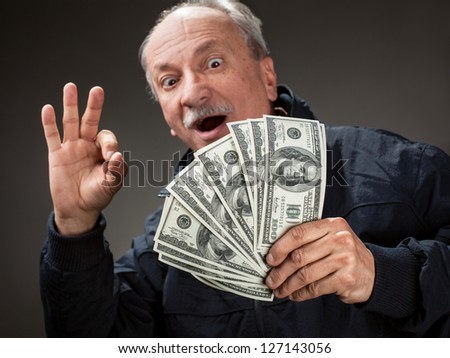 Happy elderly man showing fan of money. Focus on money. Softly blurred face