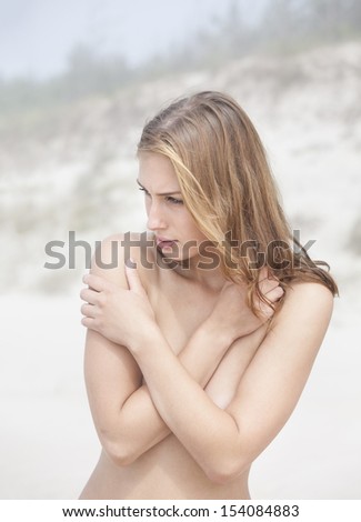 Portrait of a young naked woman on a sandy beach on a foggy day