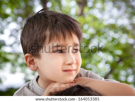 Sad little boy looking at something against blurred natural background