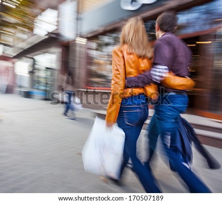Man in jeans and a woman in a leather jacket walking down the street hugging. Intentional motion blur