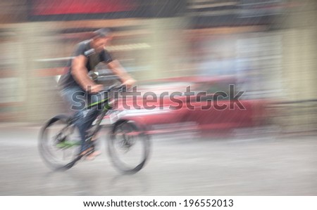 Rainfall in the city. Wet cyclist rides through the streets on a rainy day . Intentional motion blur