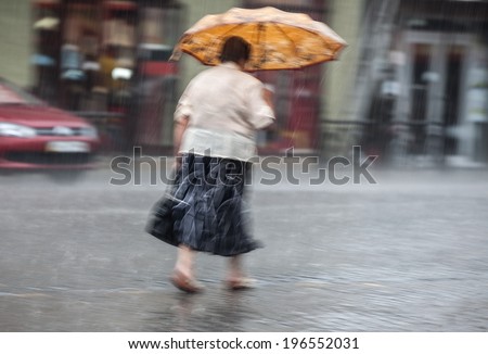 Shower. Woman walking down the street in rainy day. Intentional motion blur