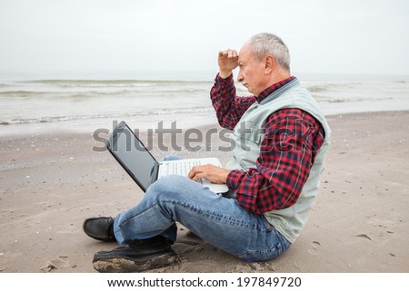 Man looks at the sea. Senior businessman sitting with notebook on beach at a foggy day