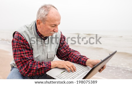Old man on the beach with a laptop on a foggy day