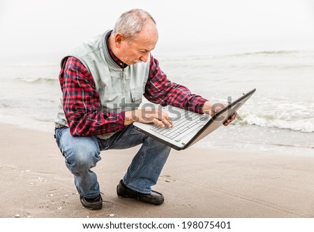 Old man sitting with notebook on beach.