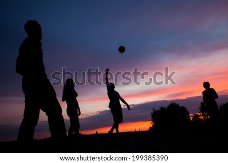 Night scene. Silhouettes of young people playing with a ball on the sunset sky background