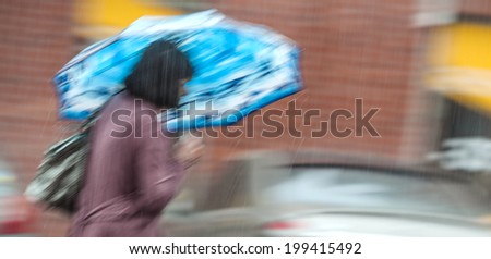 Rainfall in the city. Woman walking down the street in rainy day. Intentional motion blur