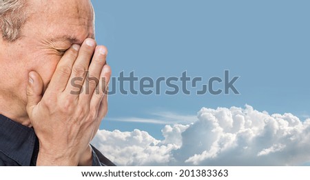 Portrait of an elderly man with face closed by hand on blue cloudy sky