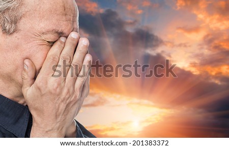 End of life\'s journey. Portrait of an elderly man with face closed by hand on sunset background