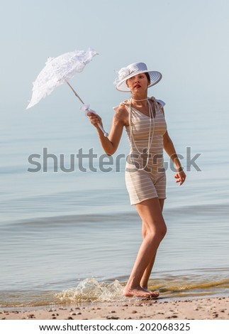 Woman in a striped retro bathing suit with a white parasol against the sea