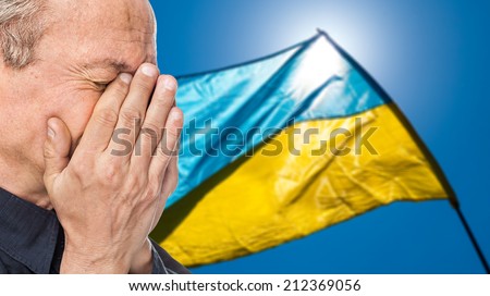 The war in Ukraine. Elderly man covered his face against of Ukrainian flag