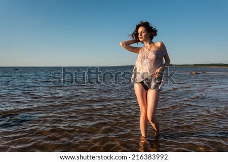 Attractive young seminude woman in a wet suit posing against the sea background