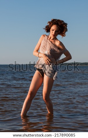 Attractive young seminude woman in a wet suit posing against the sea background. Evening light with deep shadows and color shift