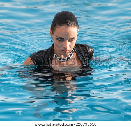 Stylish young wet woman in black dress standing in the water in a swimming pool