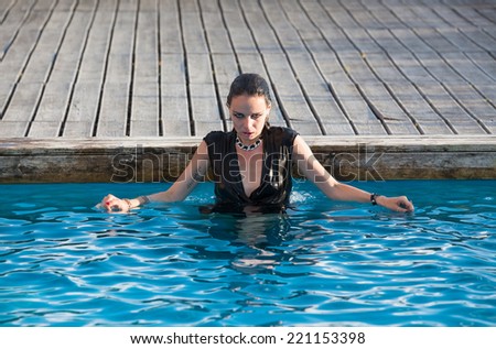 Stylish young wet woman in black dress standing in the water in a swimming pool