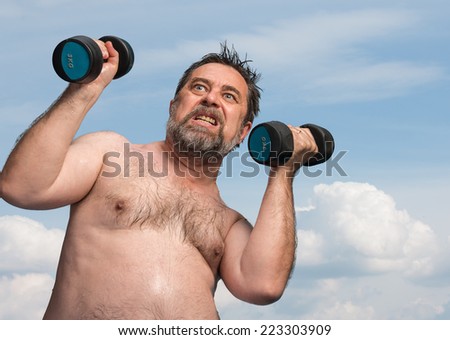 Elderly man exercising with dumbbells against the blue sky with clouds