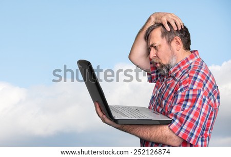 Problems with computer. Middle aged stressed businessman working on laptop against the blue sky with clouds