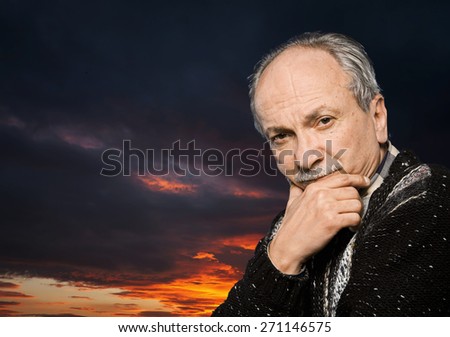 Portrait of handsome senior man prop up the head with his hand on sunset sky background