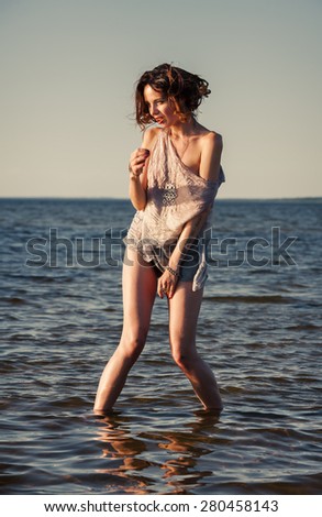 Attractive young seminude woman in a wet suit posing against the sea background