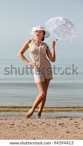 Woman in a striped retro bathing suit with a white umbrella against the sea