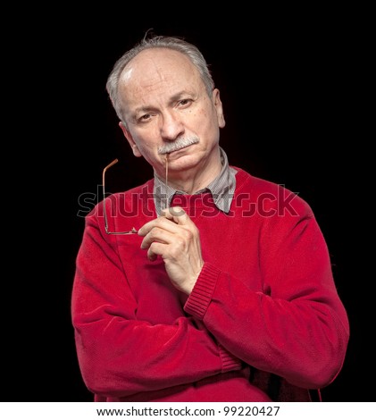 Portrait of an thoughtful  elderly man with glasses in his hands on a dark  background