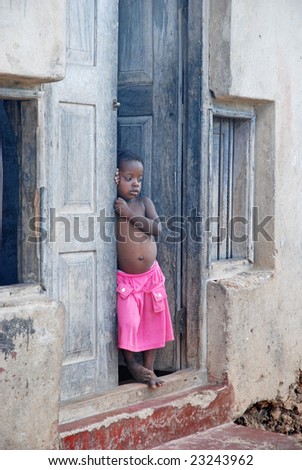 WASSINI ISLAND, KENYA, AFRICA, DECEMBER 2008: A little African girl stands in door of her family house in a poor fishermen\'s village during visit of a humanitarian group, not interested at all.