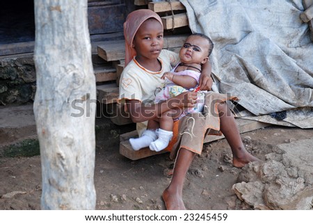 WASSINI ISLAND, KENYA, AFRICA, DECEMBER 2008: Little girl sits close to door of her family\'s house in a poor fishermen\'s village during visit of a humanitarian group, holding her.
