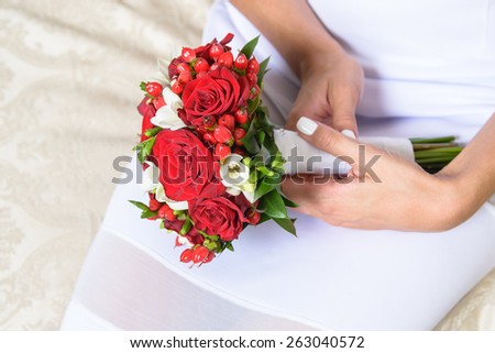 Beautiful red wedding bouquet of roses and freesia flowers in hands of the bride