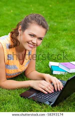 attractive caucasian girl lying on grass with laptop and smile to the camera