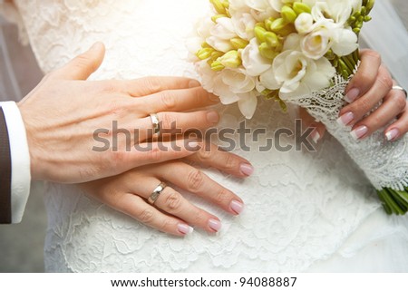 closeup of hands of bride and groom with wedding rings and bouquet