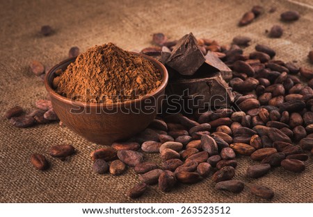 Raw cocoa beans, clay bowl  with cocoa powder, chocolate on sacking