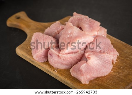 Raw fresh turkey meat on a wooden cutting board on a dark background
