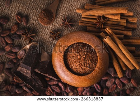 Raw cocoa beans, raw dark  homemade chocolate for rawfoodists, cinnamon sticks, star anise and cocoa powder in a wooden bowl, top view