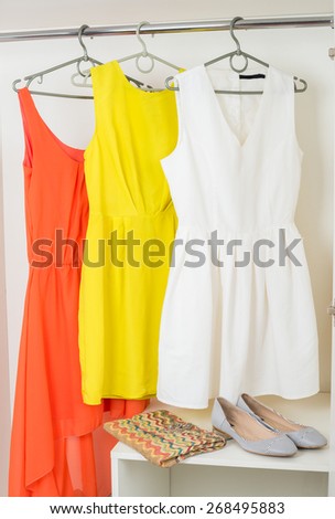 row of  bright colorful female dresses hanging on coat hanger, shoes and handbag in white wardrobe