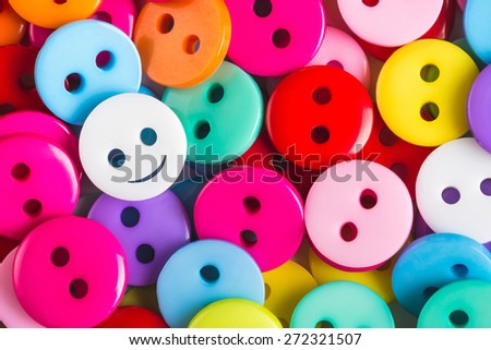 bright multicolored buttons of red, yellow, blue, orange, pink color, among them the white button - smiley stands out among other, top view,  background