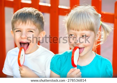 Funny children with candy lollipops, happy little blonde girl with blue eyes and little boy in a blue T-shirts eating big sugar lollipops, children eating  sweets in the park on the playground