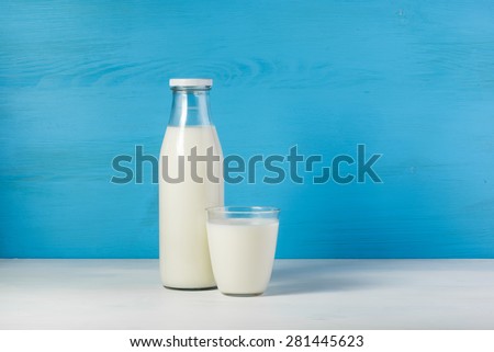 A bottle of rustic milk and glass of milk on a white table on a blue background, tasty, nutritious and healthy dairy products
