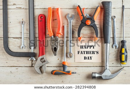 Greeting Card to Happy Father\'s Day, concept, set of different tools: a hammer, Hand saw, pliers, wrench, screwdriver, various spanners, clamp on a wooden background and text , closeup, top view
