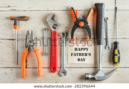 Greeting Card to Happy Father\'s Day, concept, set of different tools: a hammer, pliers, wrench, screwdriver, various spanners, clamp on a wooden background and tablet for  inscription, text, top view