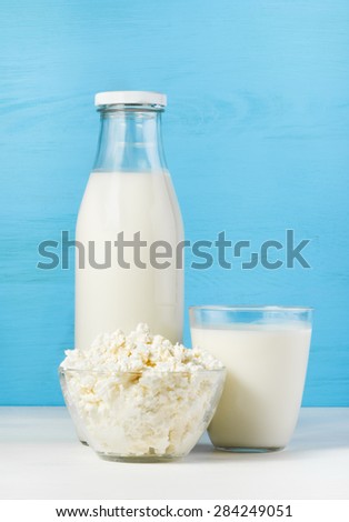tasty healthy dairy products on a white table on a blue background:  cottage cheese in bowl,  milk in a glass bottle and in a glass