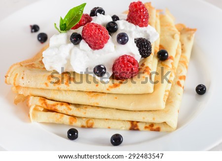 Delicious sweet crepes decorated air cream and ripe berries, raspberries, blackberries and blueberries on a white plate. Tasty breakfast.