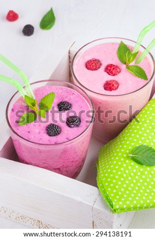 Raspberry and blackberry dairy smoothies with fresh berries and sprigs of mint in a decorative white box on a white wooden table