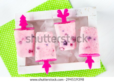 Homemade ice cream, frozen yogurt with blackberries, blueberries and raspberries, white wooden box with ice, bright green napkin in white polka dots print on a white table, top view