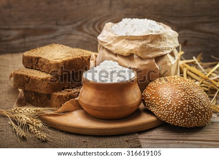 Wheat flour, sliced bread, bun with sesame seeds, wheat ears and straw on an old wooden background