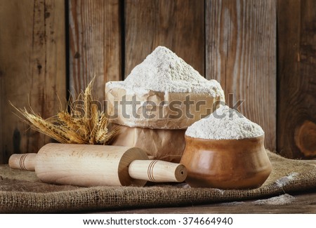 Natural, organic, wholegrain wheat meal in a paper bag, a rolling pin, wheat ears on an old wooden background