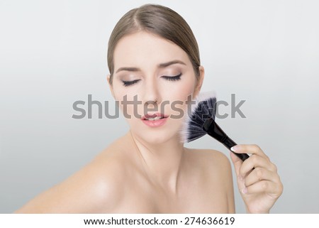Makeup blonde woman holding a makeup brush on her face