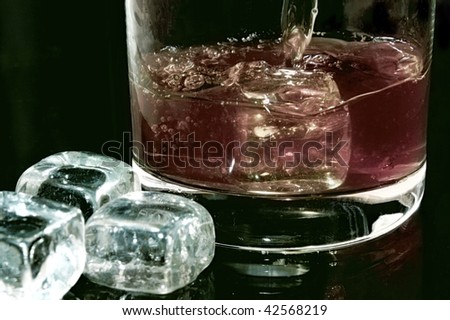 Whiskey flows into a glass with ice cubes to the right against black background in the horizontal format