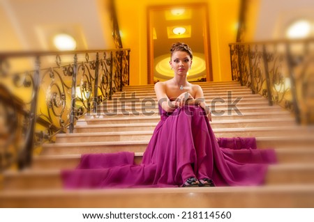 young woman in a long dress on the stairs in the hotel lobby